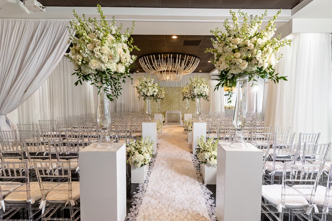 All-white ceremony with a petal-lined aisle beneath the rope chandelier