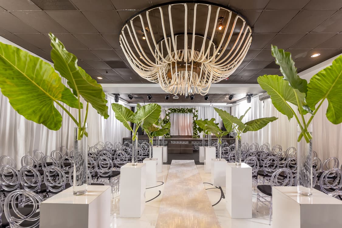 Ceremony styled with tropical leaves beneath the rope chandelier