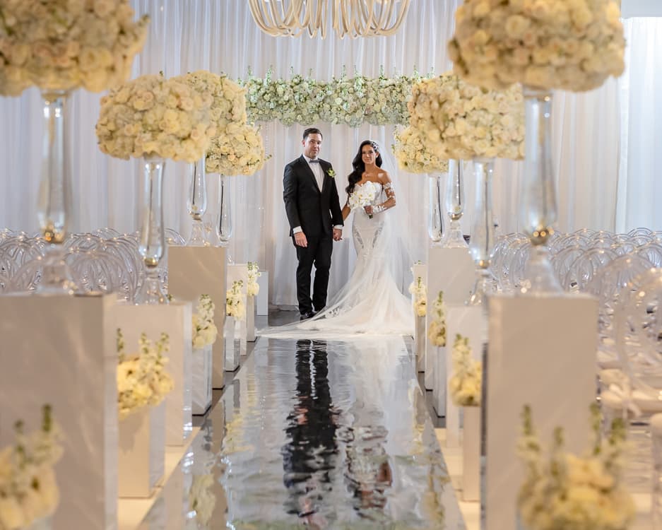 Bride and groom on the mirrored aisle surrounded by white florals