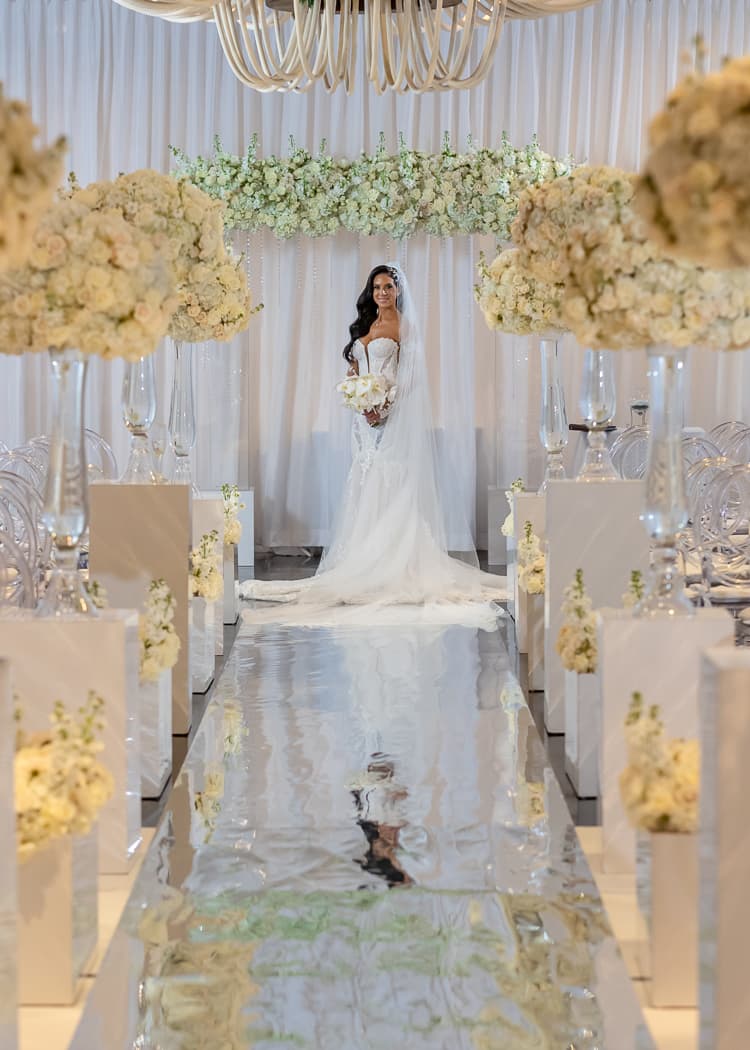 Bride standing on the mirrored ceremony aisle beneath the chandelier