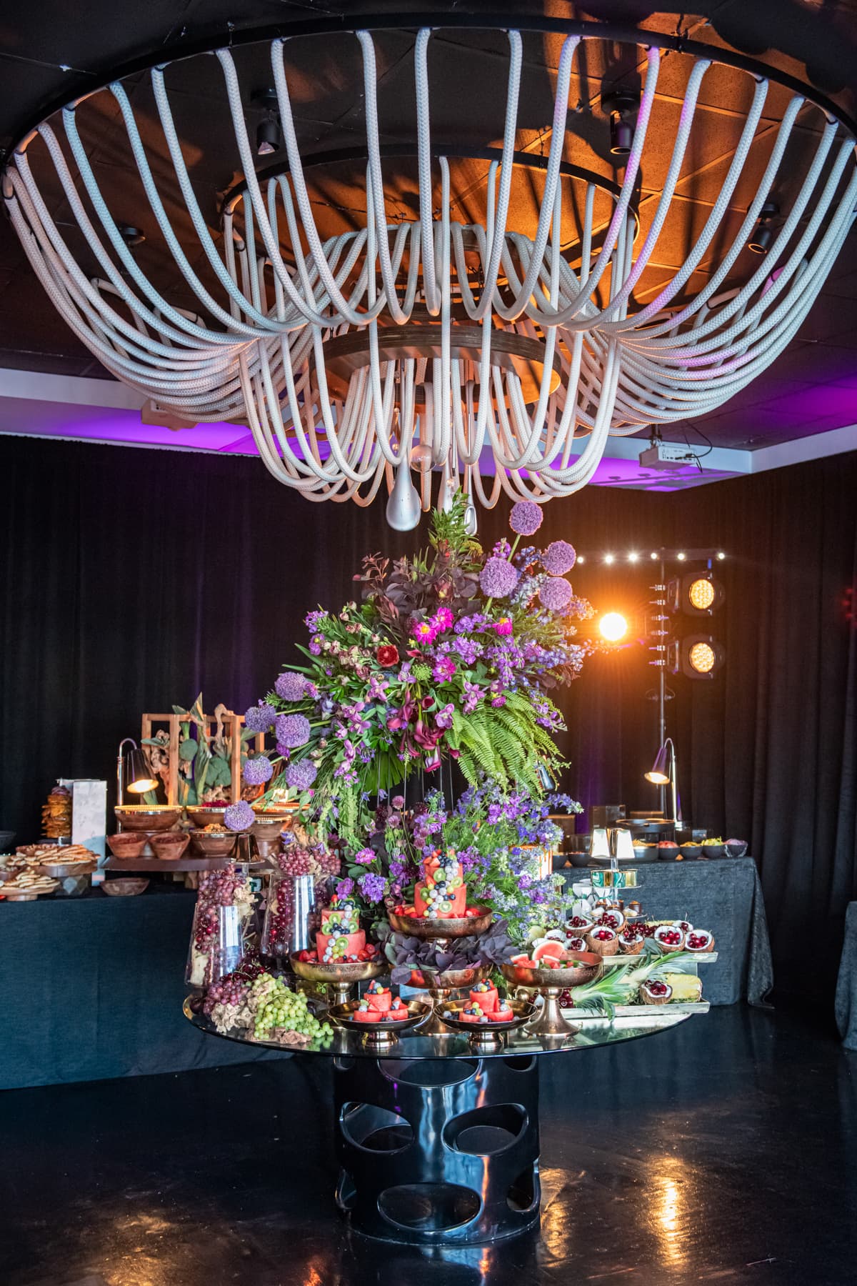 Fruit and dessert display crowned with florals beneath the rope chandelier